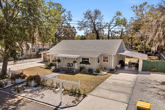 view of front facade featuring an attached carport, roof with shingles, covered porch, concrete driveway, and a fenced front yard