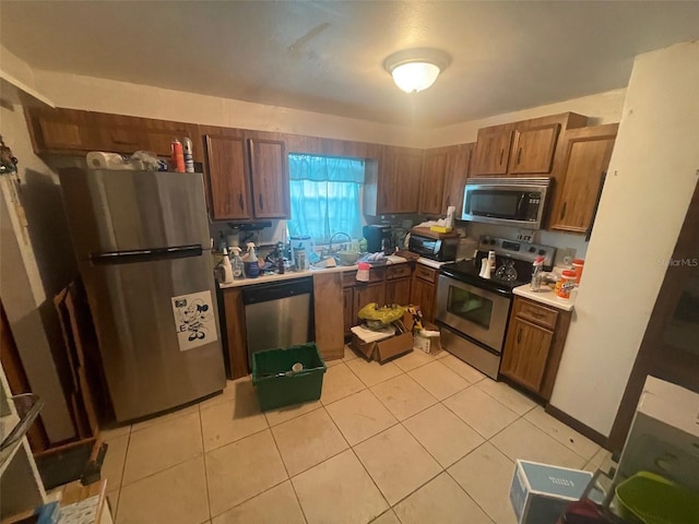 kitchen featuring a sink, appliances with stainless steel finishes, brown cabinetry, light countertops, and light tile patterned floors