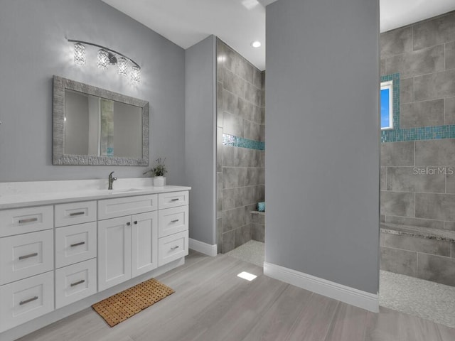 full bath with a walk in shower, vanity, baseboards, and wood finished floors