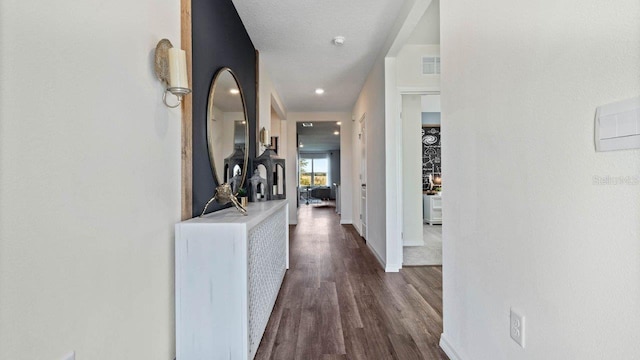 hallway with dark wood-style floors, visible vents, a textured ceiling, and baseboards