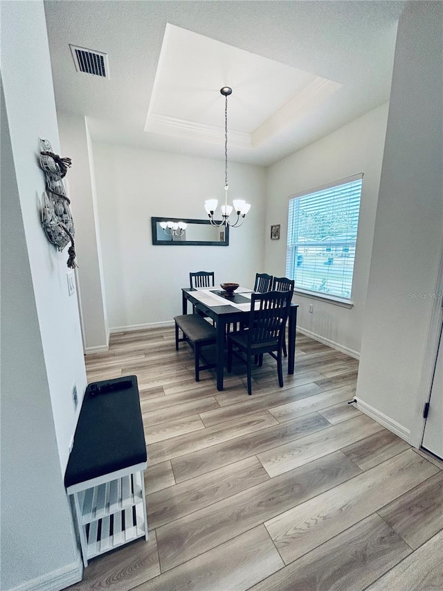 dining space with a chandelier, visible vents, light wood-style flooring, and a raised ceiling