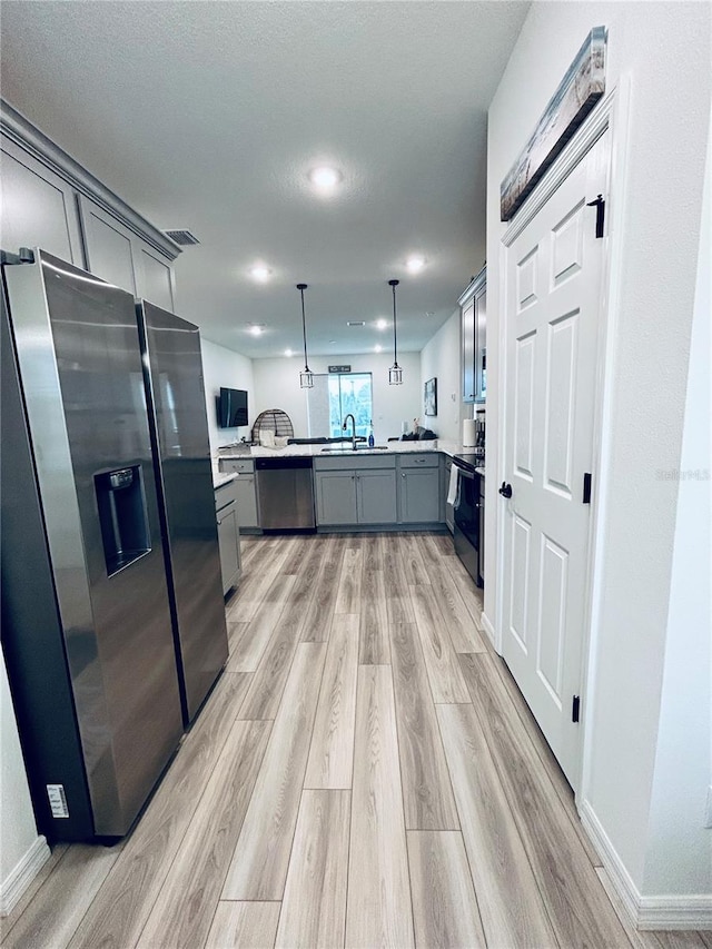 kitchen with a peninsula, gray cabinets, a sink, stainless steel appliances, and light wood-style floors