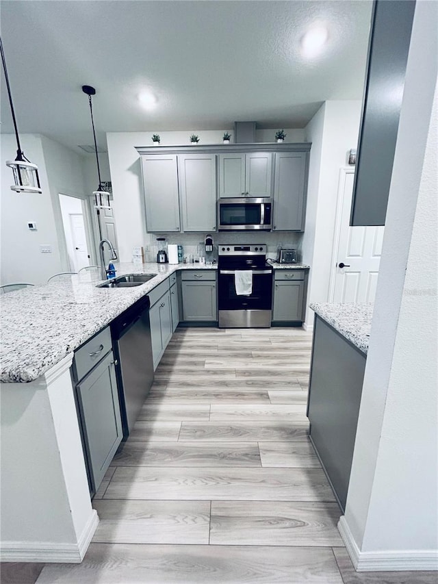 kitchen featuring light wood-type flooring, gray cabinets, a sink, stainless steel appliances, and a peninsula