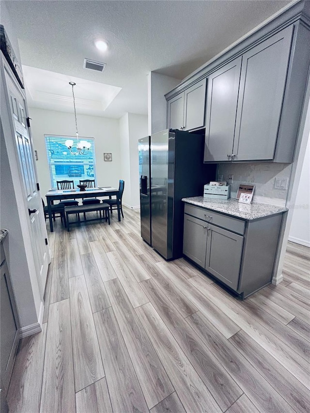 kitchen featuring visible vents, gray cabinetry, stainless steel fridge with ice dispenser, light wood-type flooring, and a tray ceiling