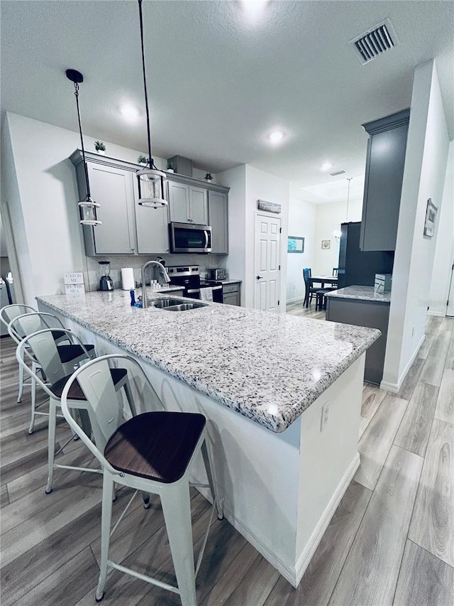 kitchen with light stone counters, visible vents, a peninsula, light wood-style floors, and appliances with stainless steel finishes