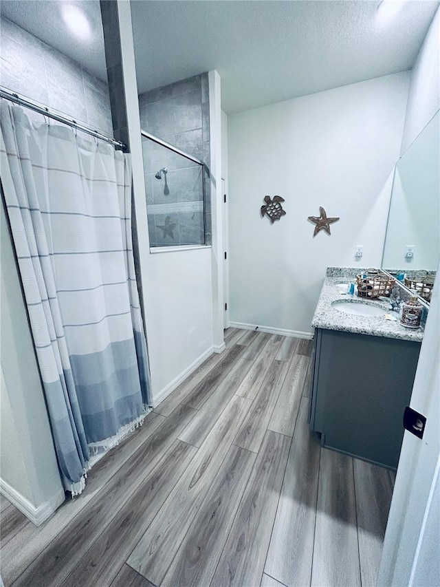 full bathroom with vanity, wood finished floors, baseboards, and a tile shower