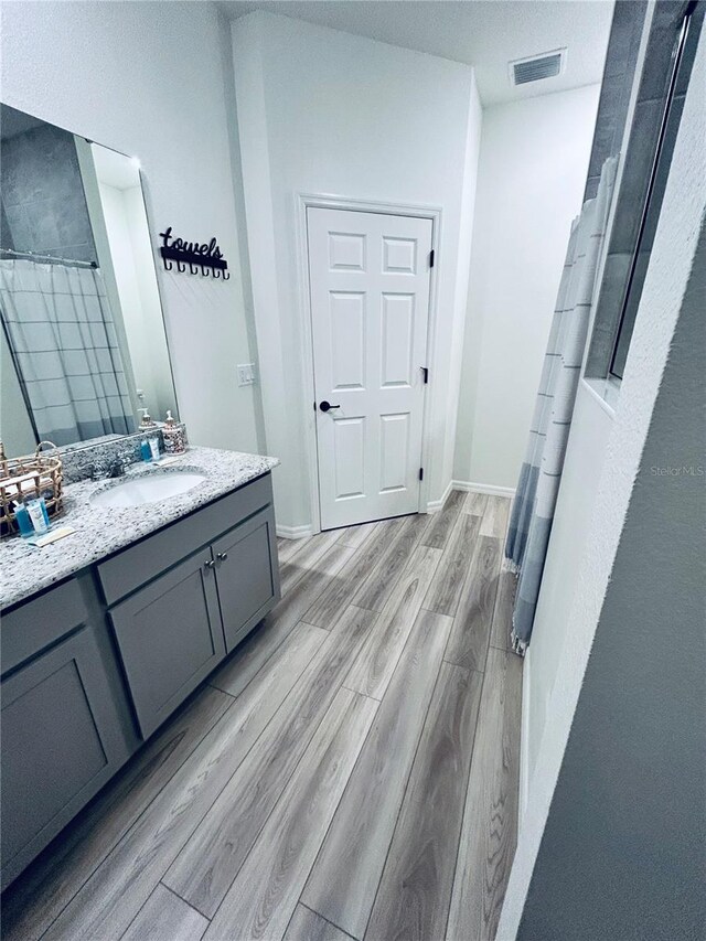 full bath with vanity, a shower with shower curtain, wood finished floors, visible vents, and baseboards
