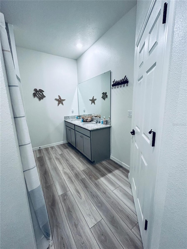 bathroom featuring wood finished floors, baseboards, double vanity, a sink, and a textured ceiling