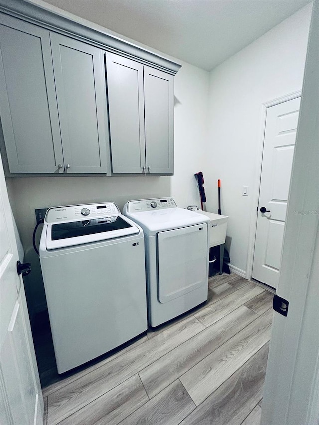 laundry room featuring baseboards, light wood-style flooring, separate washer and dryer, cabinet space, and a sink