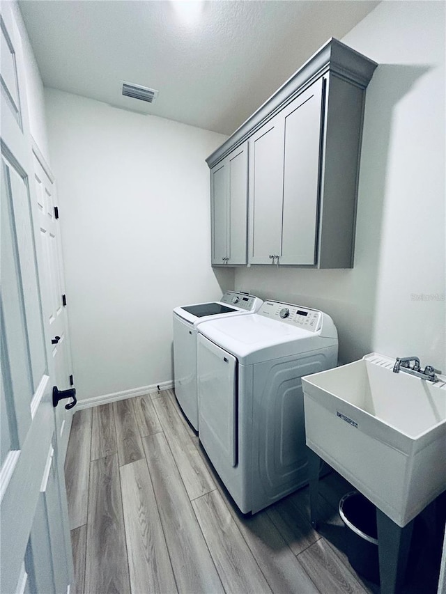 washroom with visible vents, cabinet space, a sink, light wood-style floors, and washer and clothes dryer