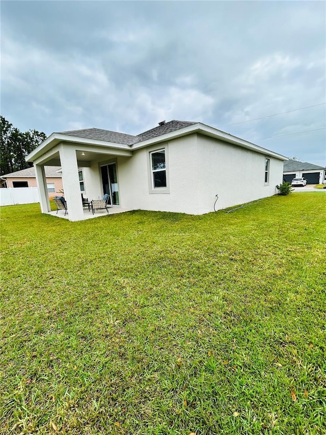 rear view of property featuring fence, roof with shingles, stucco siding, a yard, and a patio area