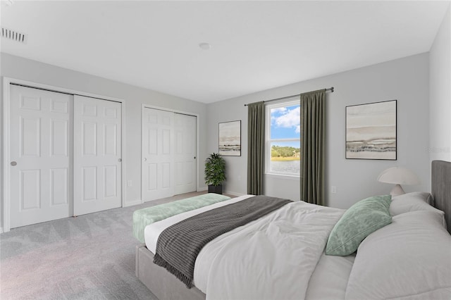 bedroom with visible vents, baseboards, two closets, and carpet