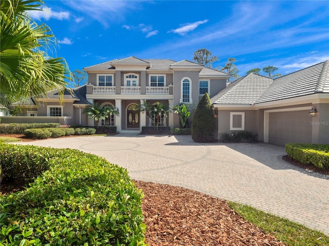 mediterranean / spanish-style house featuring a balcony, decorative driveway, an attached garage, and stucco siding