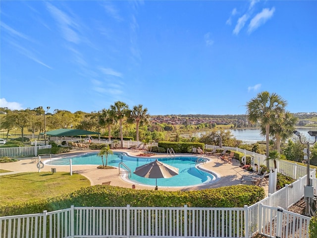 pool featuring a water view, a patio, and fence