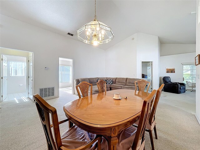 dining room with light carpet, visible vents, high vaulted ceiling, and a chandelier