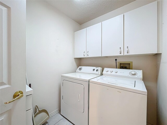 clothes washing area featuring washing machine and clothes dryer, cabinet space, and a textured ceiling