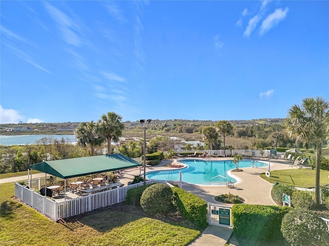 community pool with a yard, a water view, a patio, and fence