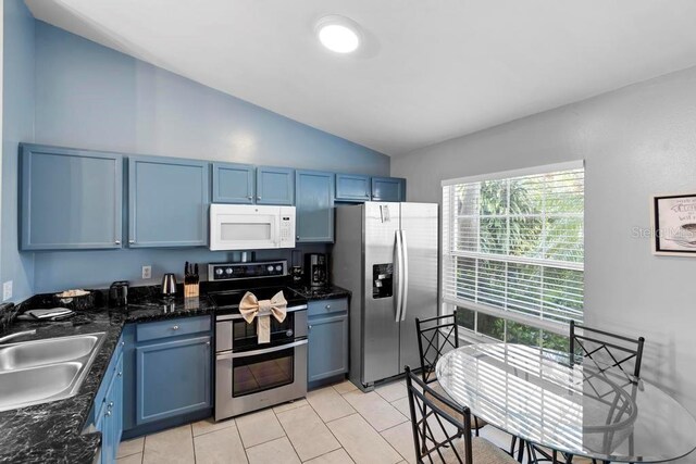 kitchen with blue cabinetry, light tile patterned flooring, a sink, vaulted ceiling, and appliances with stainless steel finishes