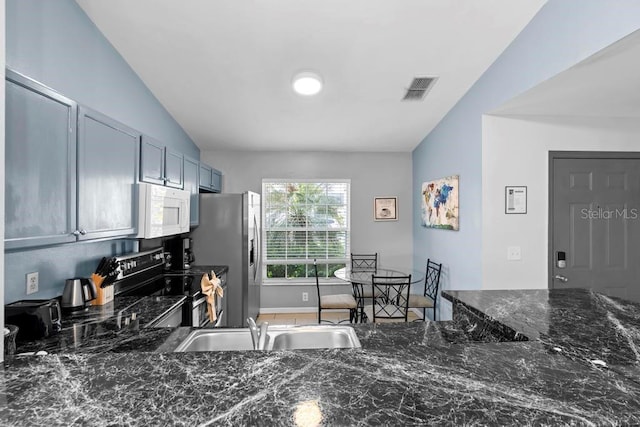 kitchen with visible vents, a sink, dark stone counters, appliances with stainless steel finishes, and vaulted ceiling