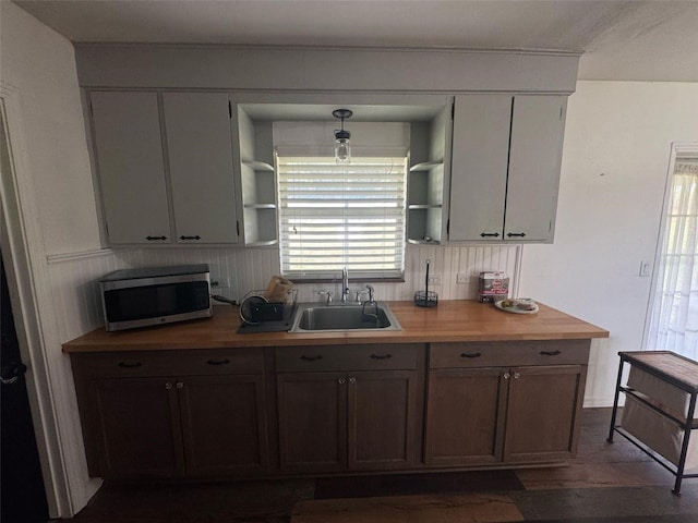 kitchen with a sink, stainless steel microwave, open shelves, and butcher block countertops