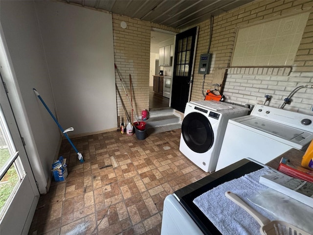 clothes washing area with laundry area, washing machine and dryer, brick floor, and brick wall