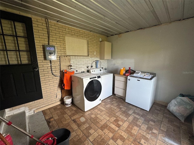 clothes washing area with brick floor, brick wall, and washer and clothes dryer