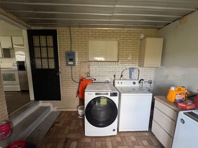 clothes washing area with washer and dryer, cabinet space, electric panel, and brick wall