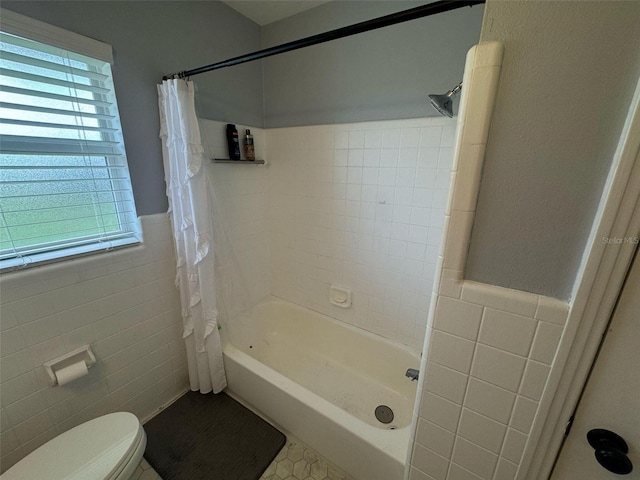 full bath featuring tile walls, toilet, shower / bathtub combination with curtain, and wainscoting