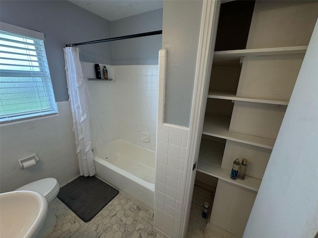 full bathroom featuring tile patterned floors, shower / bath combo with shower curtain, toilet, tile walls, and wainscoting