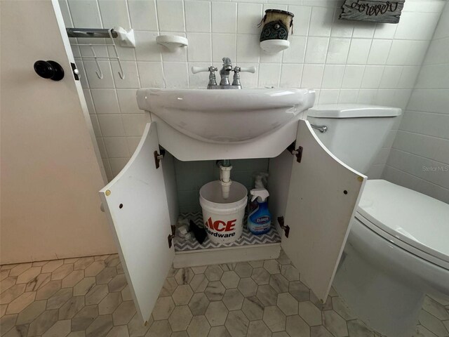 half bath featuring tile patterned flooring, tile walls, toilet, and a sink