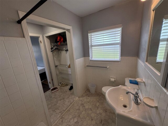 bathroom with tile patterned flooring, a wainscoted wall, toilet, tile walls, and a sink