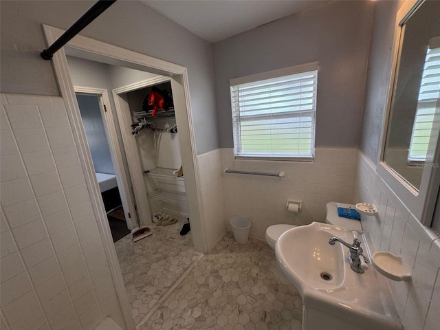 bathroom featuring a walk in closet, tile walls, toilet, and a wainscoted wall