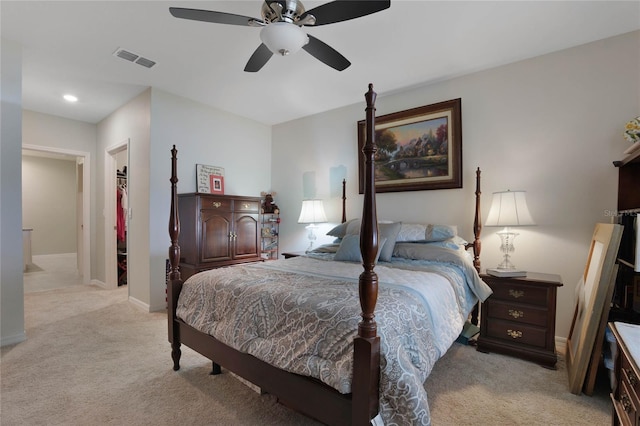 bedroom featuring visible vents, a walk in closet, baseboards, light colored carpet, and ceiling fan