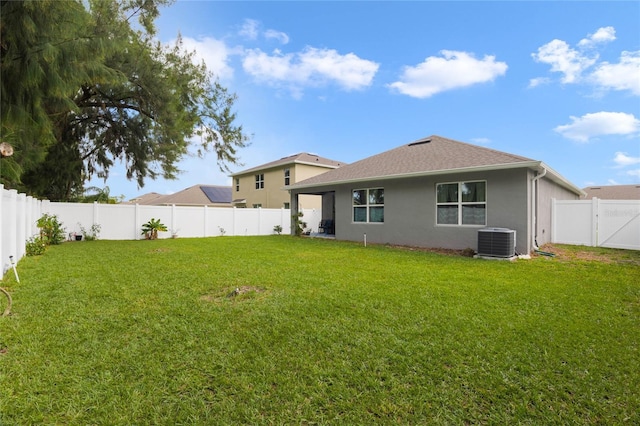 back of house with stucco siding, a lawn, central AC, a fenced backyard, and roof with shingles