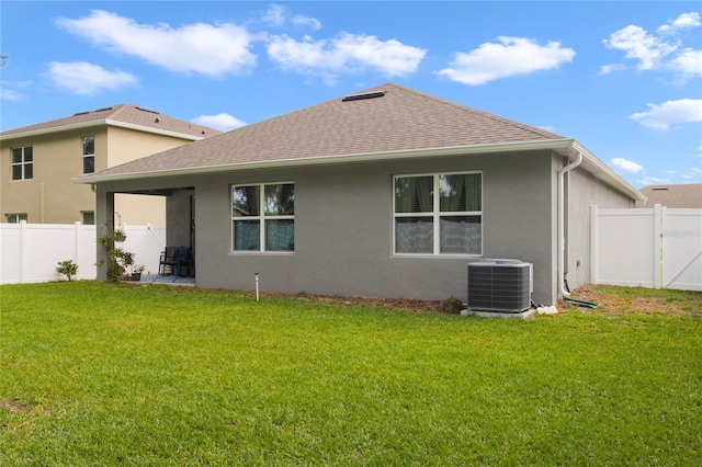 back of house featuring a lawn, a fenced backyard, central AC, and stucco siding