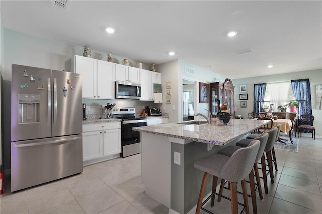 kitchen with visible vents, a breakfast bar, a sink, stainless steel appliances, and white cabinets