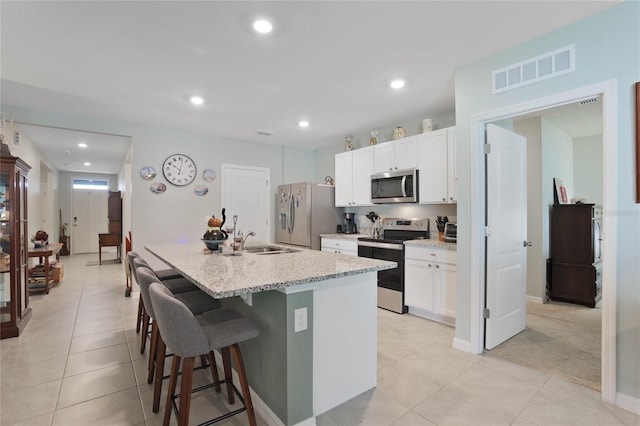 kitchen featuring a center island with sink, visible vents, a sink, appliances with stainless steel finishes, and a kitchen breakfast bar