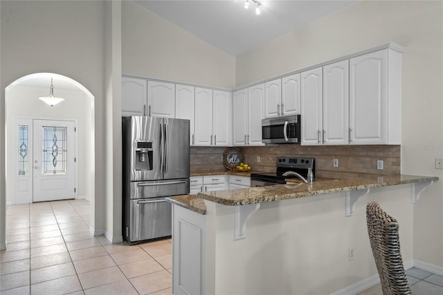 kitchen featuring stone countertops, backsplash, stainless steel appliances, arched walkways, and a peninsula