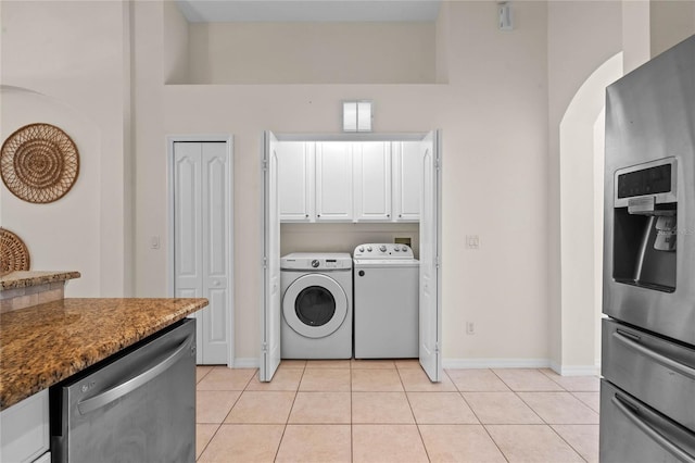 laundry room featuring baseboards, arched walkways, light tile patterned flooring, cabinet space, and separate washer and dryer