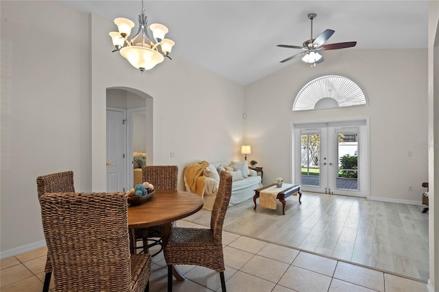 dining space with light tile patterned floors, high vaulted ceiling, arched walkways, french doors, and ceiling fan with notable chandelier