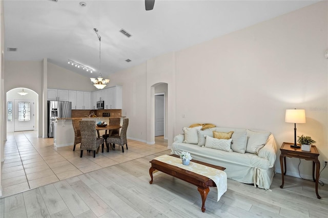 living area featuring light wood-style floors, visible vents, arched walkways, and high vaulted ceiling