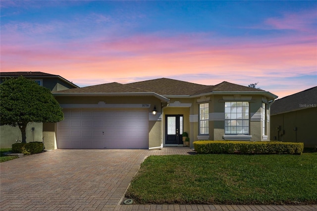 prairie-style house with stucco siding, decorative driveway, a garage, and a front yard