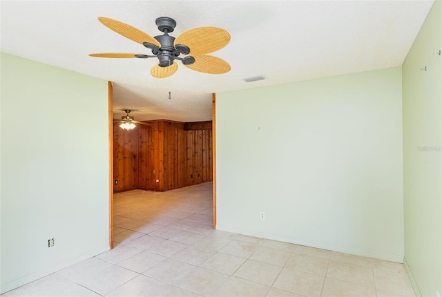 unfurnished room with visible vents, wood walls, light tile patterned floors, baseboards, and ceiling fan