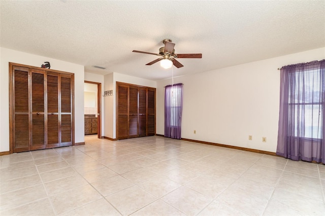 unfurnished bedroom with visible vents, baseboards, multiple closets, light tile patterned floors, and a textured ceiling