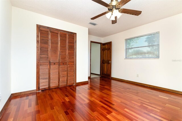 unfurnished bedroom featuring visible vents, baseboards, wood finished floors, a closet, and a textured ceiling