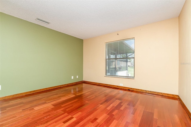 empty room featuring baseboards, wood finished floors, visible vents, and a textured ceiling