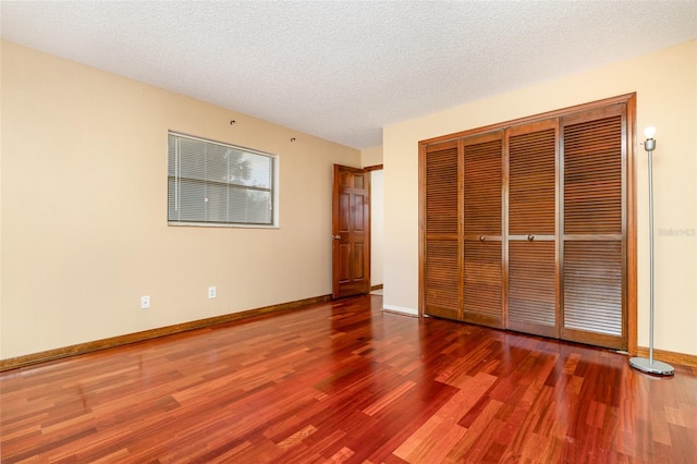 unfurnished bedroom with a closet, baseboards, a textured ceiling, and wood finished floors