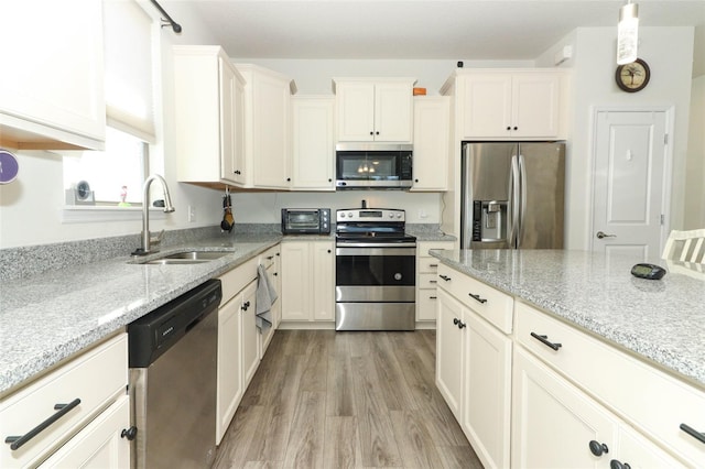 kitchen with light wood-style flooring, appliances with stainless steel finishes, light stone countertops, and a sink