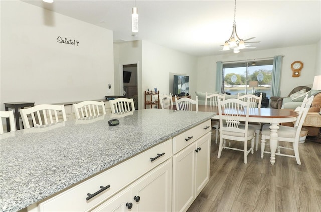 kitchen with light stone counters, wood finished floors, an inviting chandelier, hanging light fixtures, and white cabinets