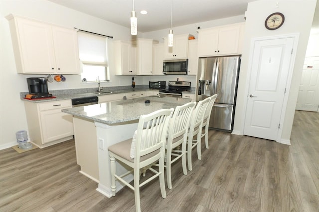 kitchen with a kitchen island, stainless steel appliances, wood finished floors, white cabinetry, and a sink